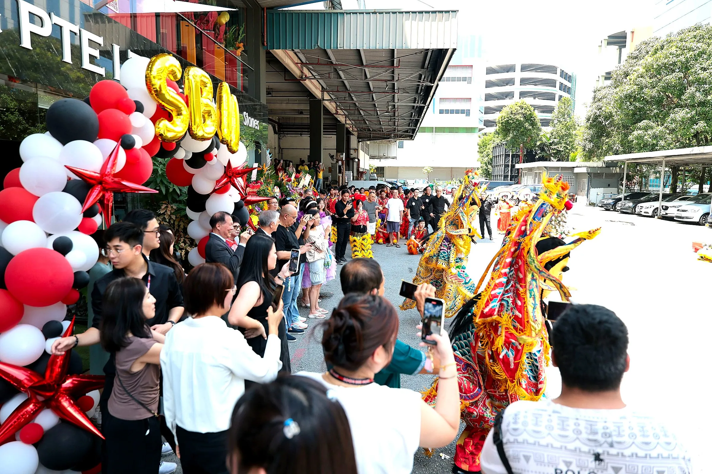 Crowd watching a lion dance outside a shop opening, framed by balloons