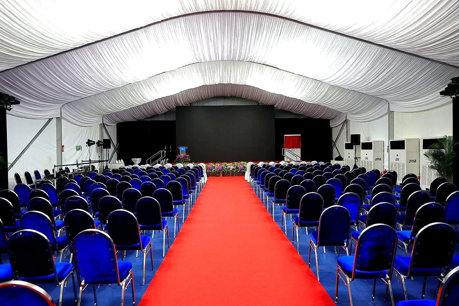 Red carpet aisle leading to a stage inside a large conference marquee